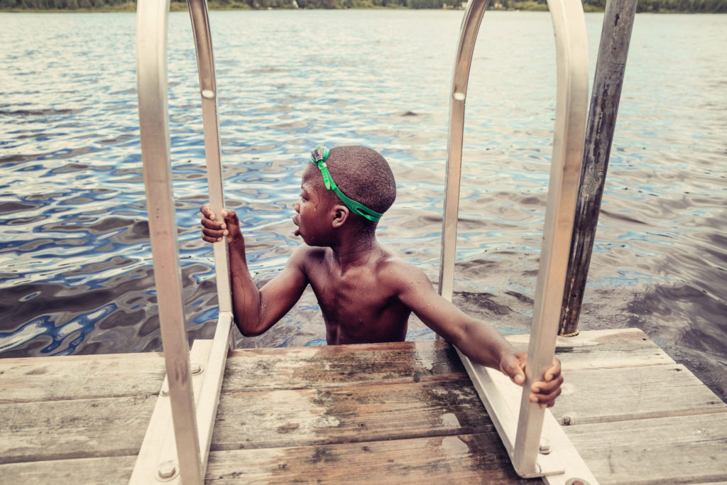 Young african-american boy with goggles swimming in lake.