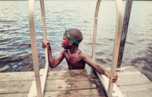 Young african-american boy with goggles swimming in lake.