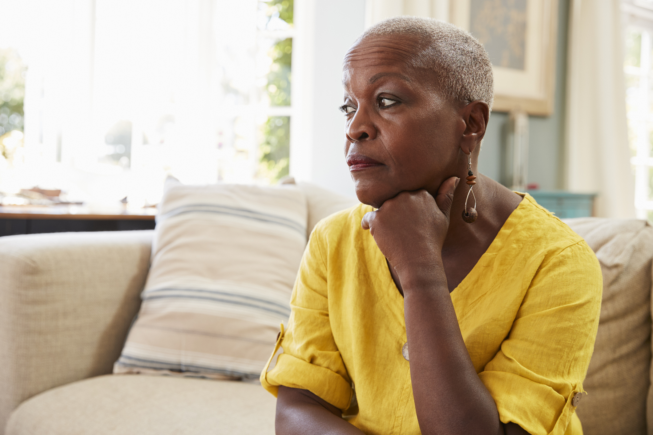 Senior Woman Sitting On Sofa At Home Suffering From Depression