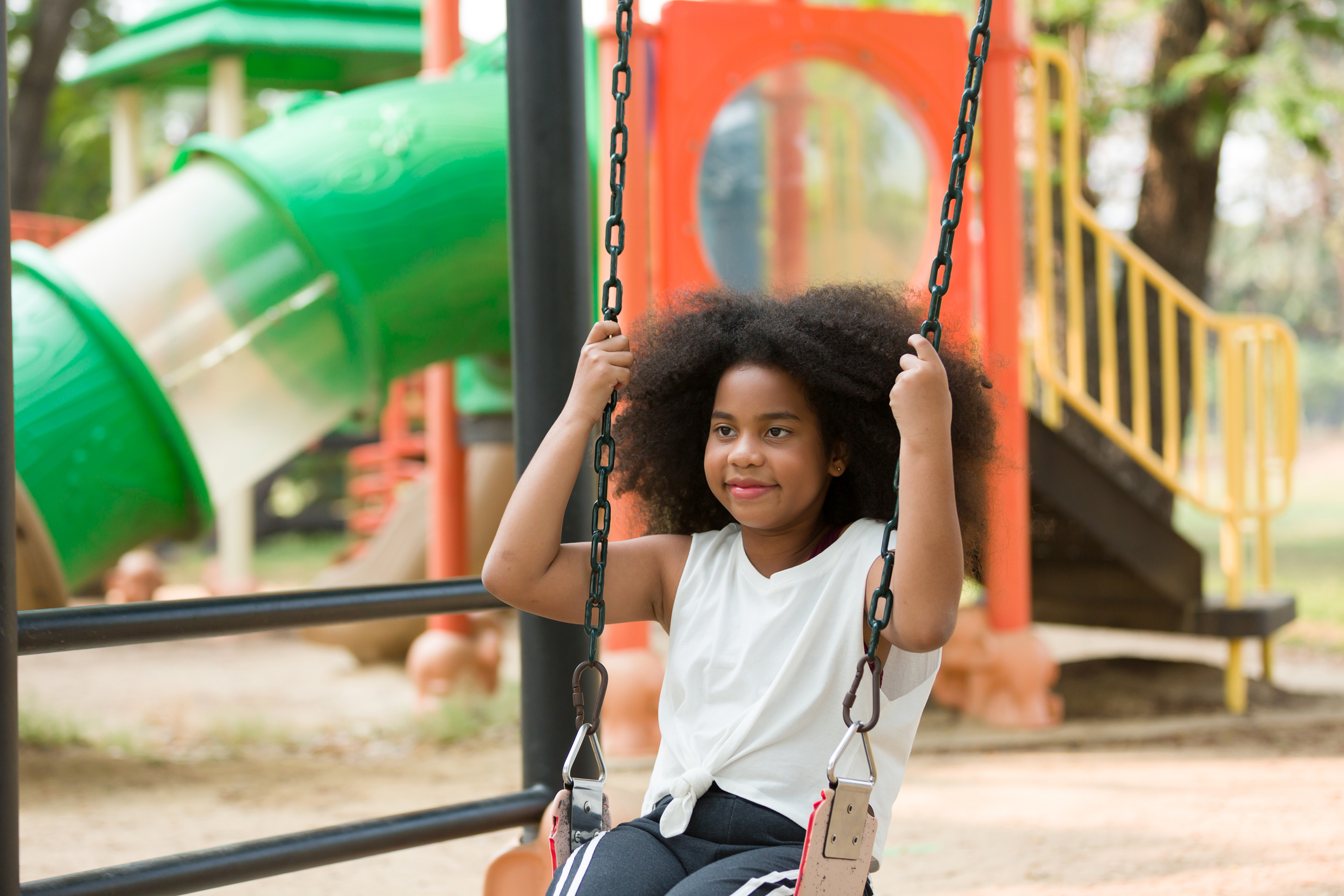 African American child curly smiling girl playing on swing at playground