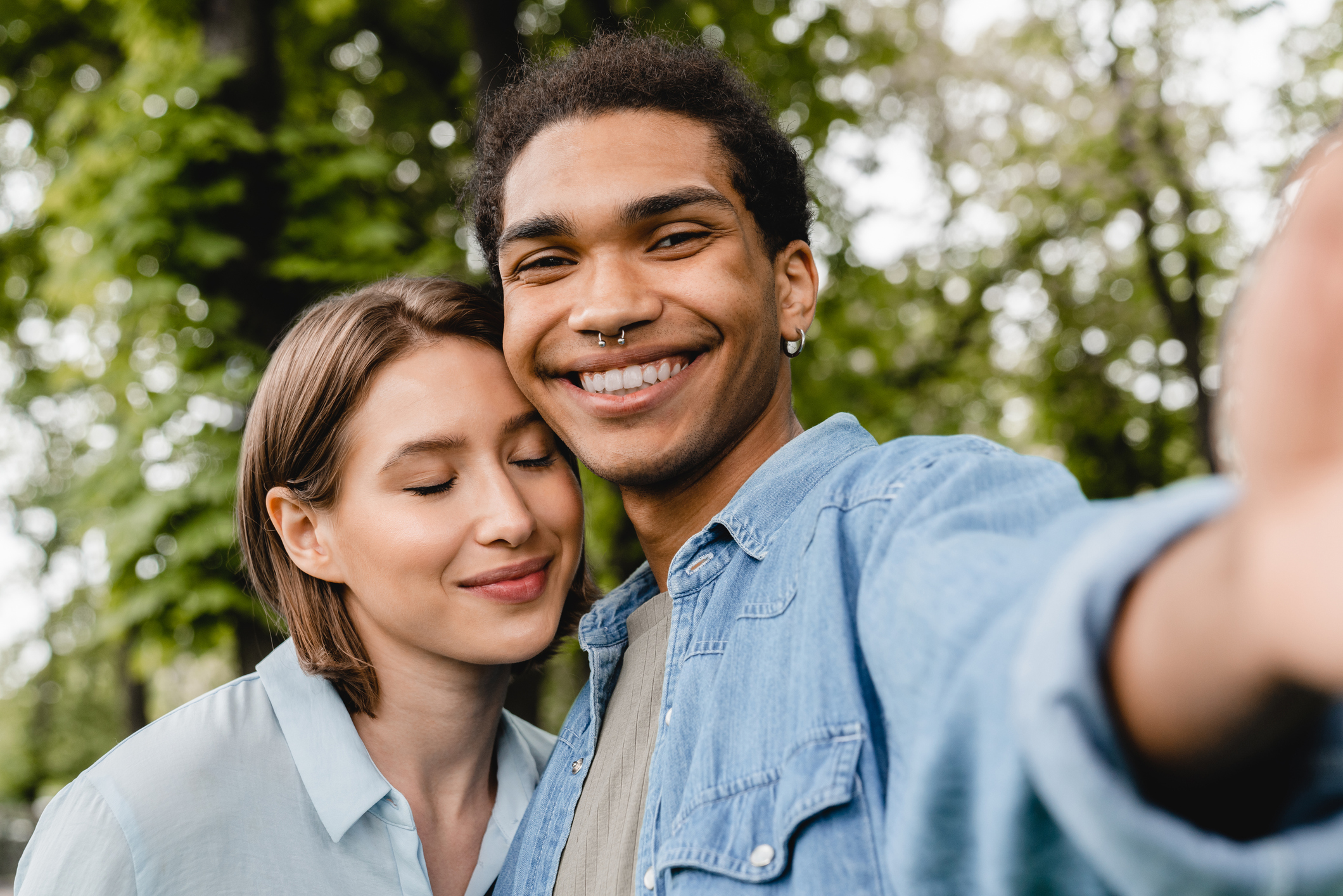 Cheerful happy young romantic couple spending time together on romantic date taking selfie on smartphone in city park. 