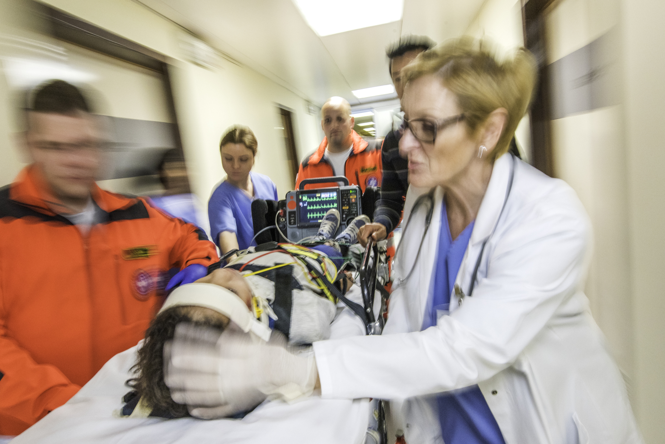 Paramedics and female doctor pulling hospital trolley.