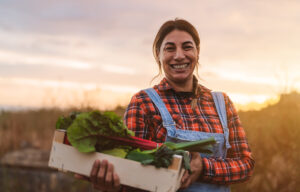 Happy female farmer holding a wood box containing fresh vegetables