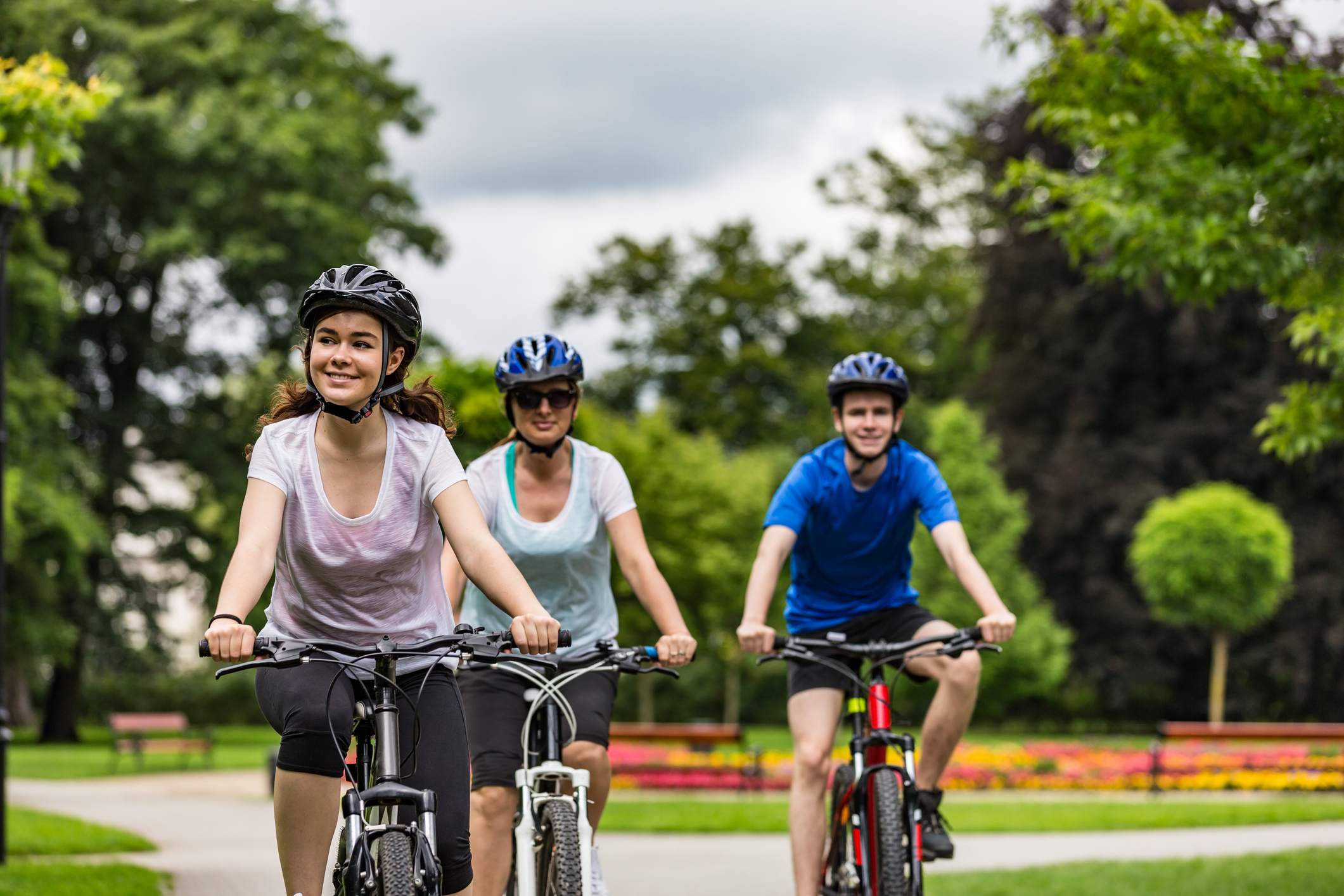 Two teens and an adult riding bicycles in city park