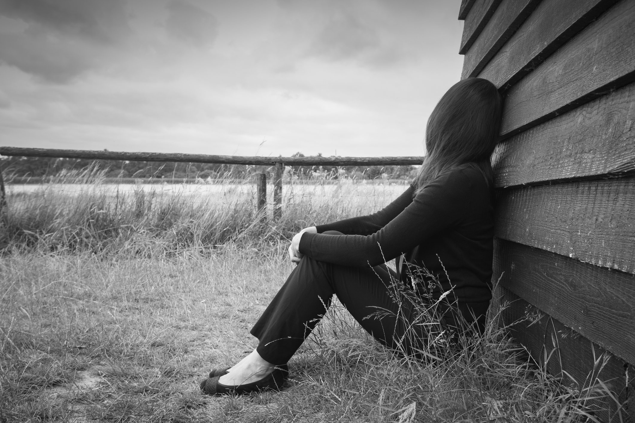 Young, sad woman leaning against a barn and gazing into the distance. 