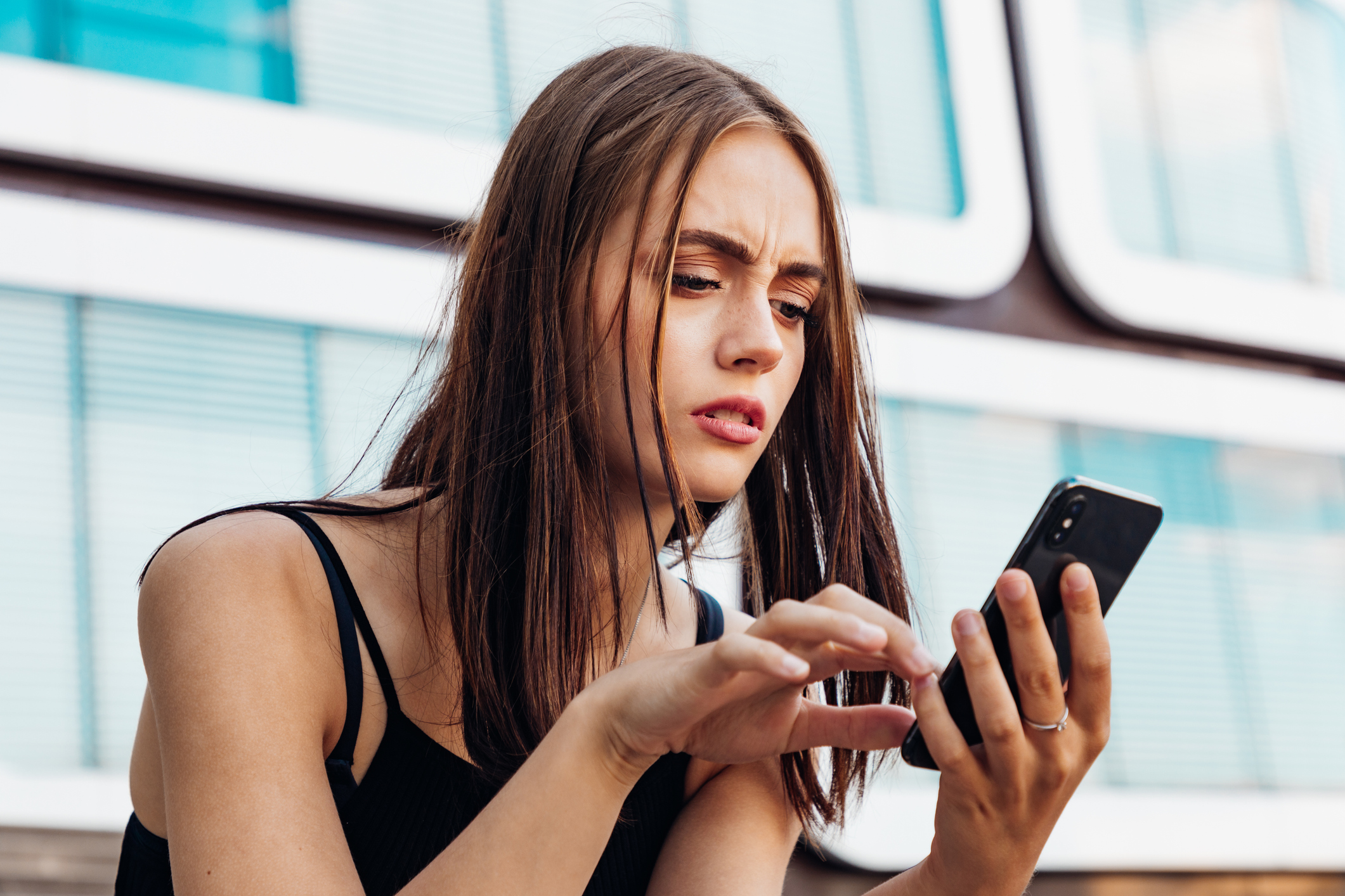 Young teenage woman checking her messages and social media post on her mobile phone. Looking worried and questioning reading the bad news and messages on her smart phone.