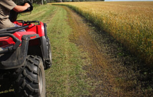 a teen on an ATV driving on a lane checking out the crop in the field