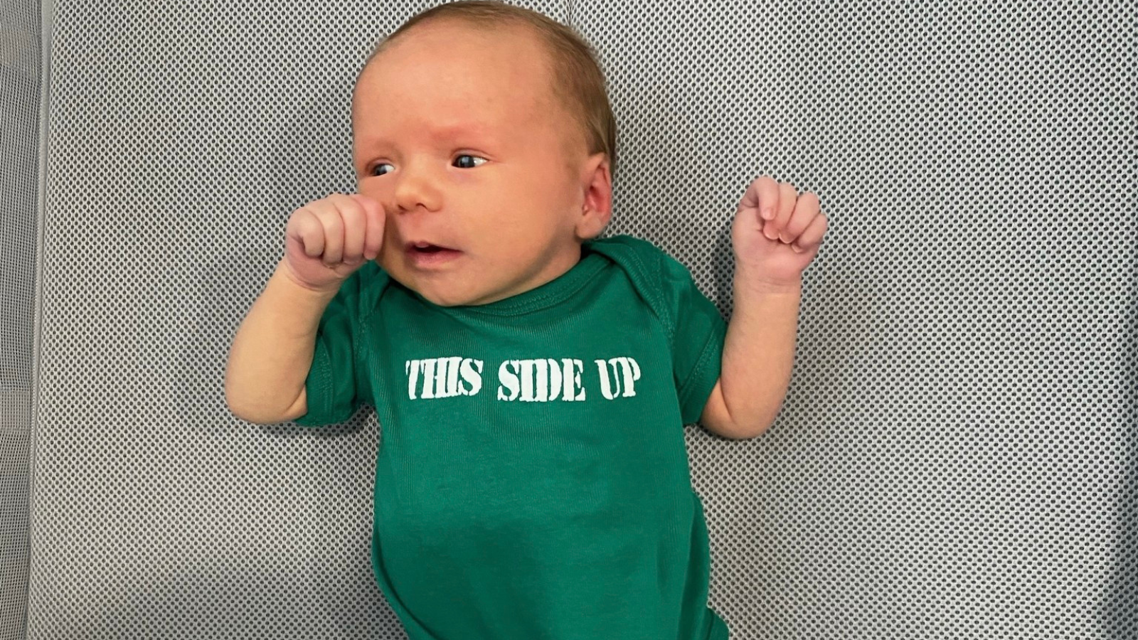 baby on her back wearing a onesie that says "This side up"