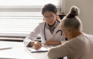 Female doctor consulting an older woman. They are sitting at a table looking at some paperwor.