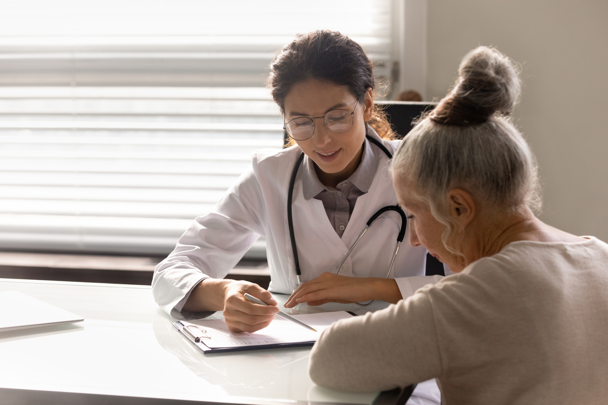 Female doctor consulting an older woman. They are sitting at a table looking at some paperwor.