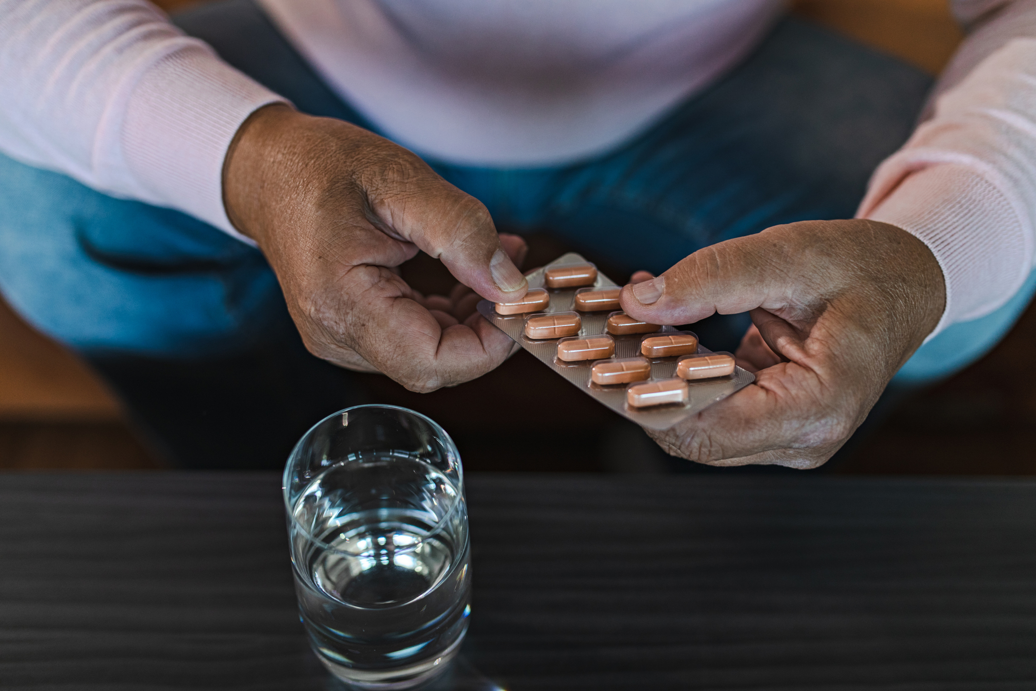 A Black man's hands holding a package of pills next to a glass of water