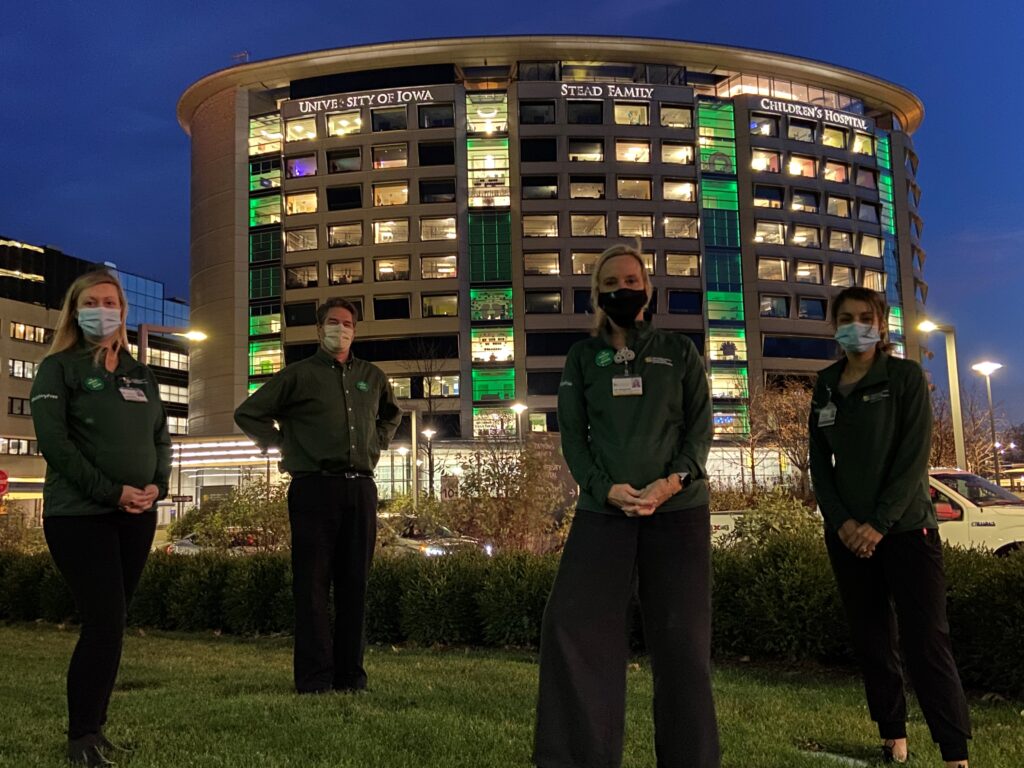 Four staff and faculty stand in front of the UI Stead family Children's Hospital lighting green for National Injury Prevention Day.