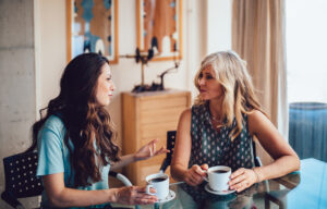 Two women drinking coffee and talking while sitting at a table