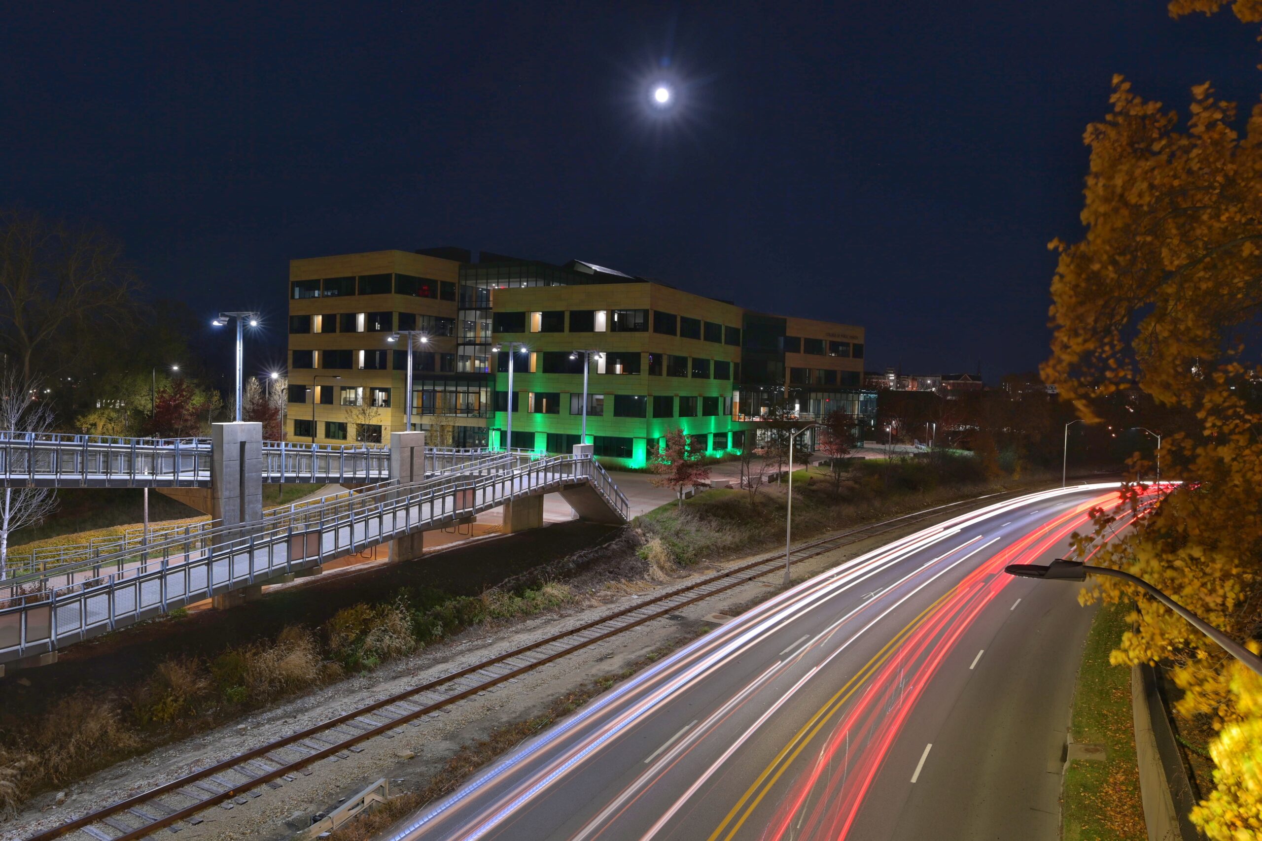 The UI COllege of Public Health building lighting green at night with view of road