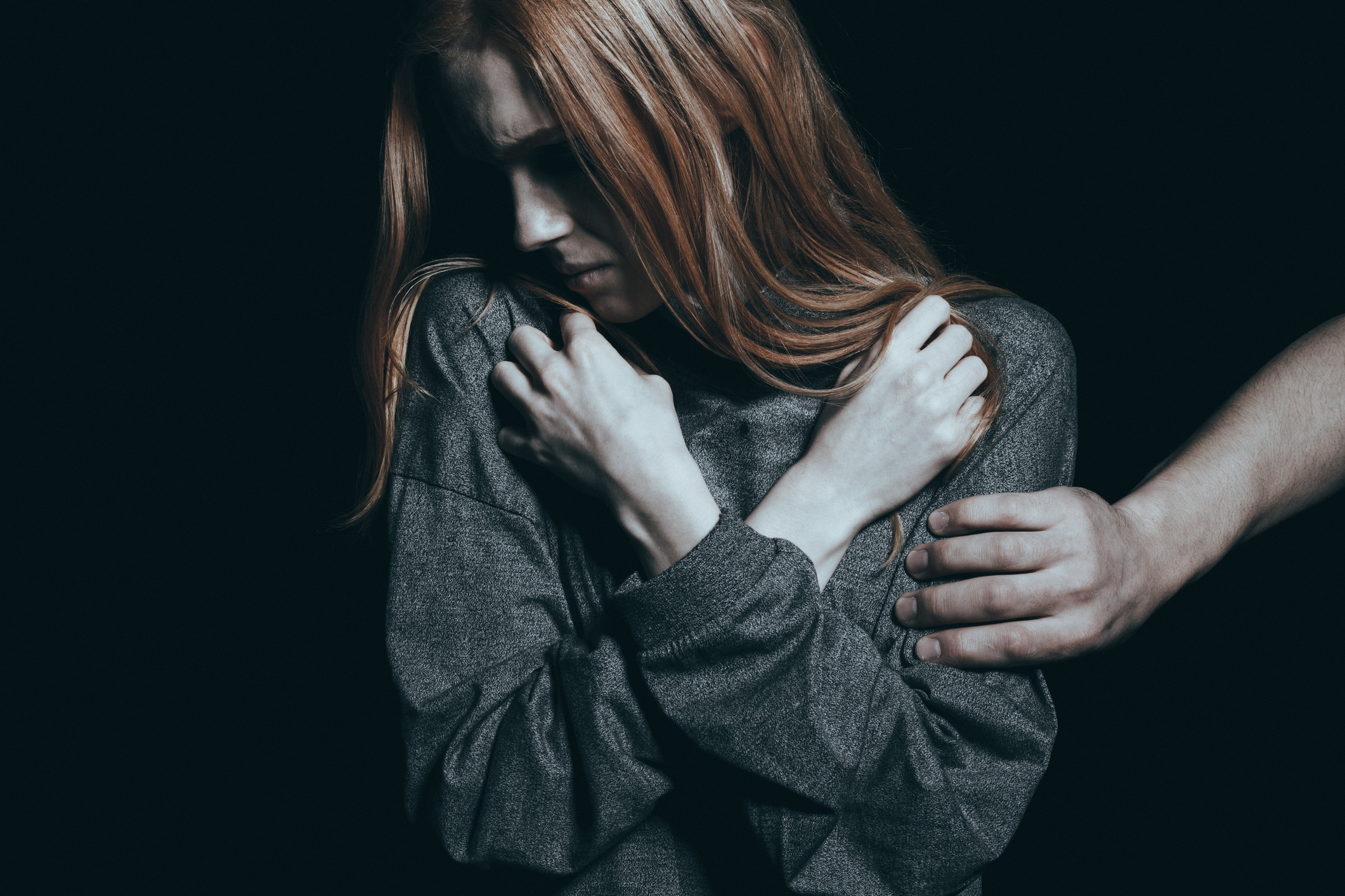 young woman shields herself with her arms crossed and head turned to the side