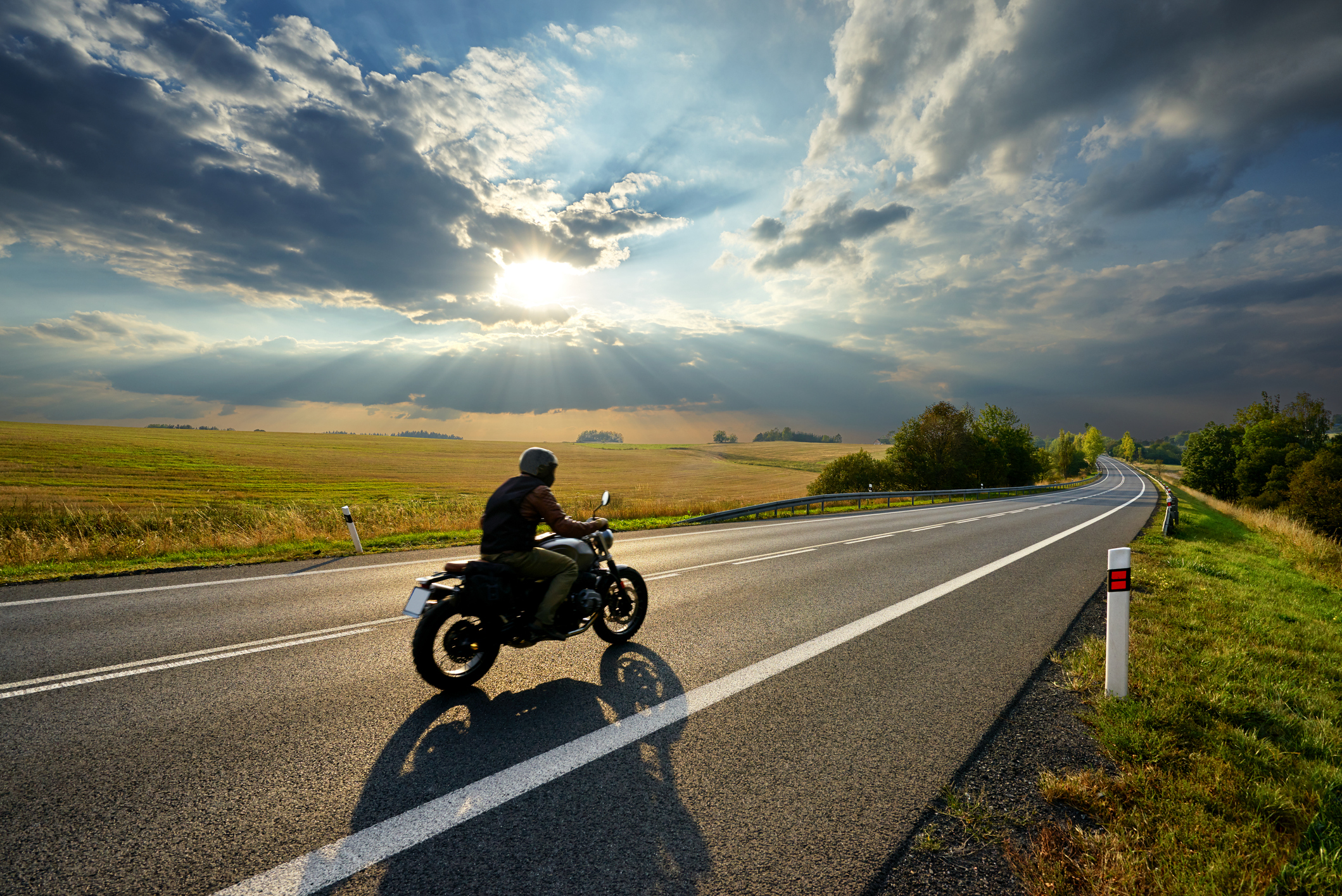 Motorcycle driving on the asphalt road in rural landscape at sunset with dramatic clouds