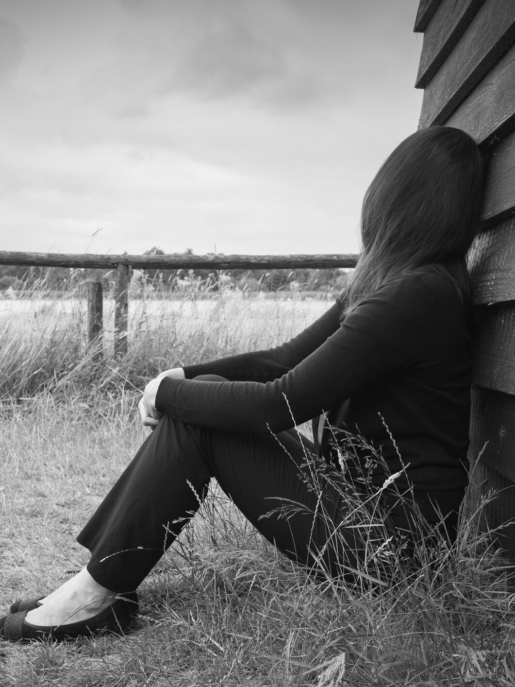 Young sad anonymous woman leaning against a hut and gazing into the distance. Monochrome portrait.