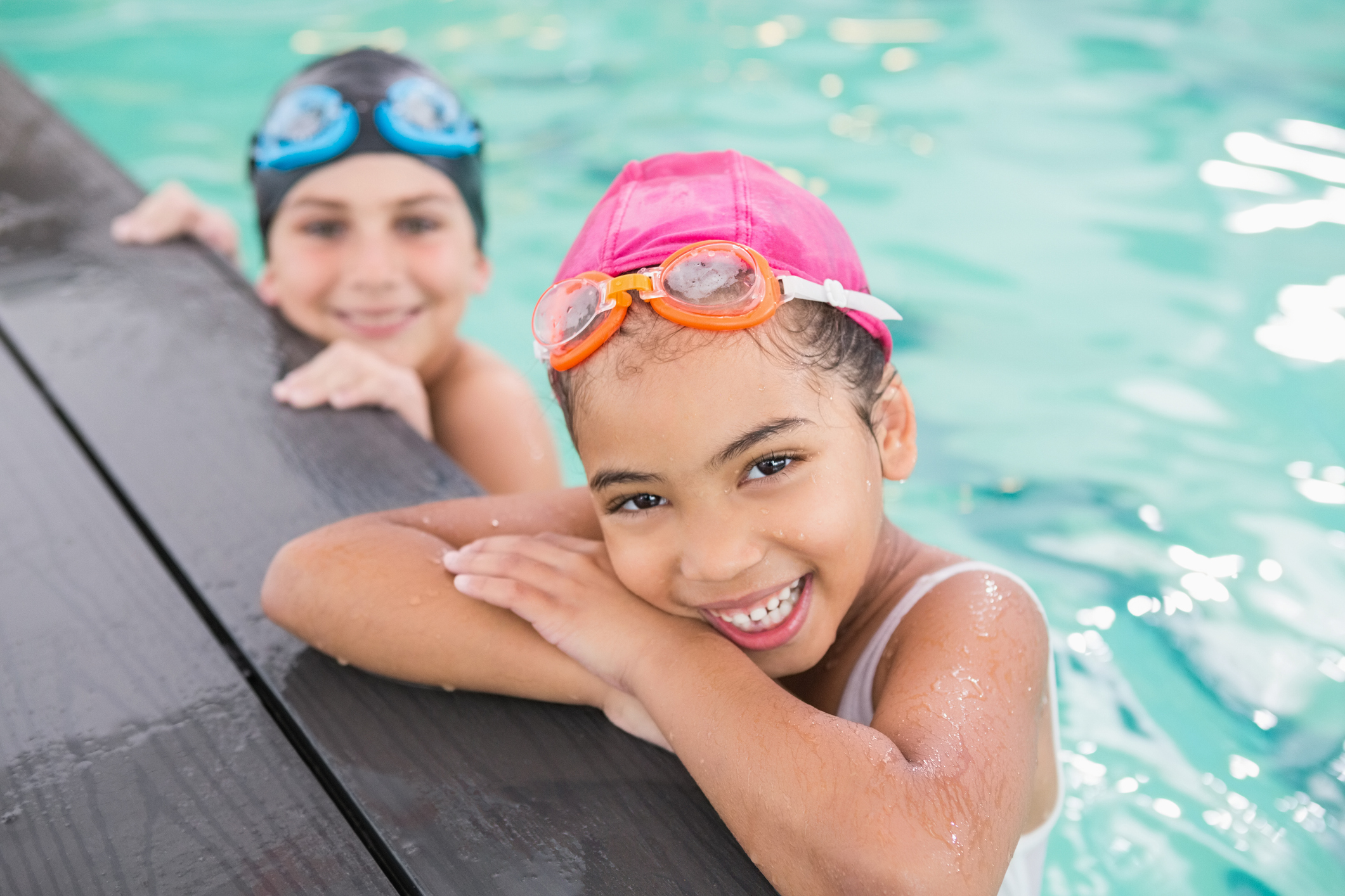 Two young girls smile at the side of a swimming pool