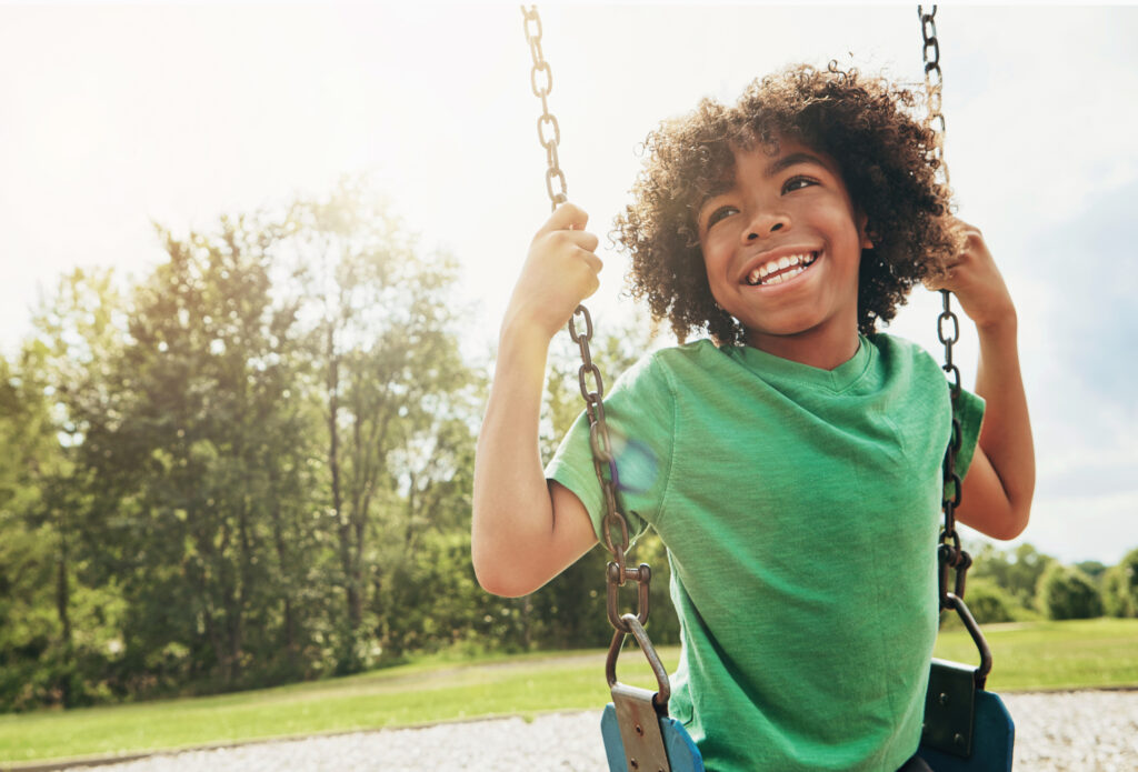 Young Black boy smiling on a swing at a park