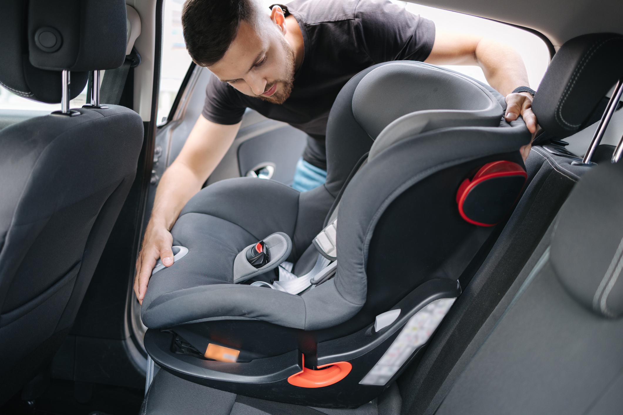 Man installs a child car seat in car at the back seat. Responsible father thought about the safety of his child