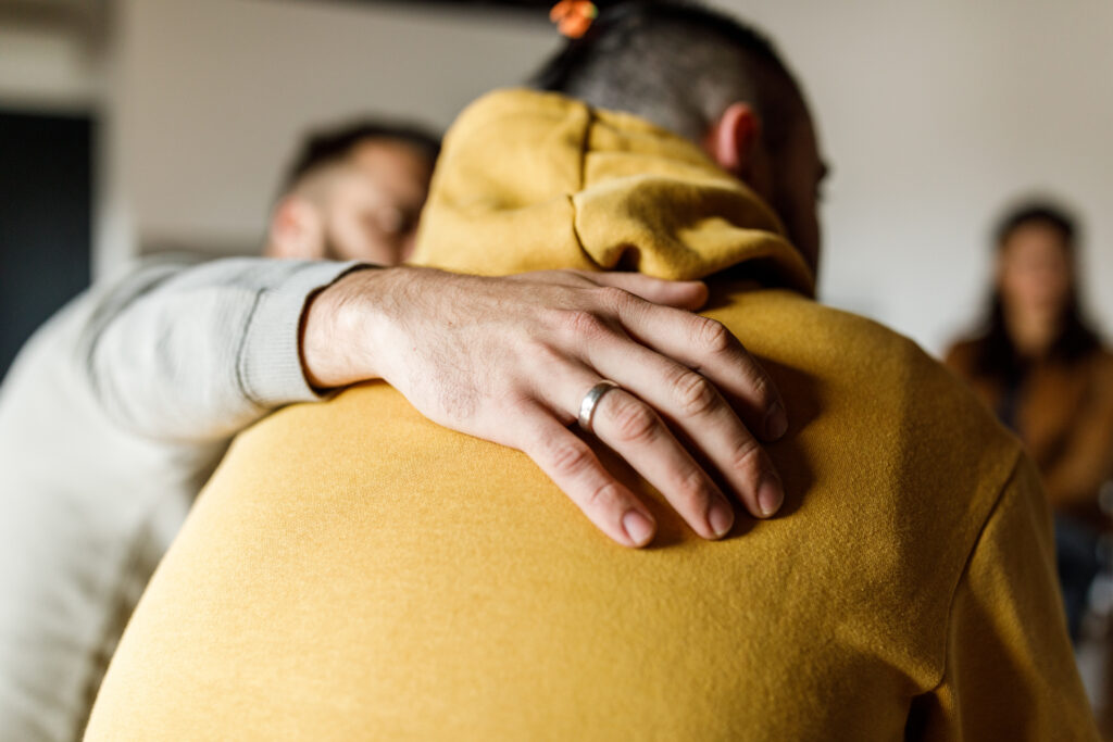 Man with his hand across the back of another man, comforting him