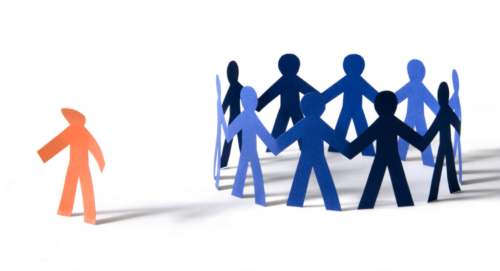 Orange paper person with dejected stance off to the side of a circle of blue paper people holding hands