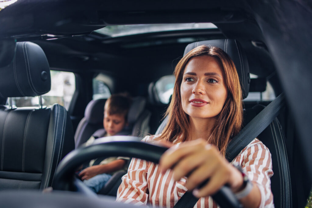 Young woman drives in car with child in car seat in back seat.