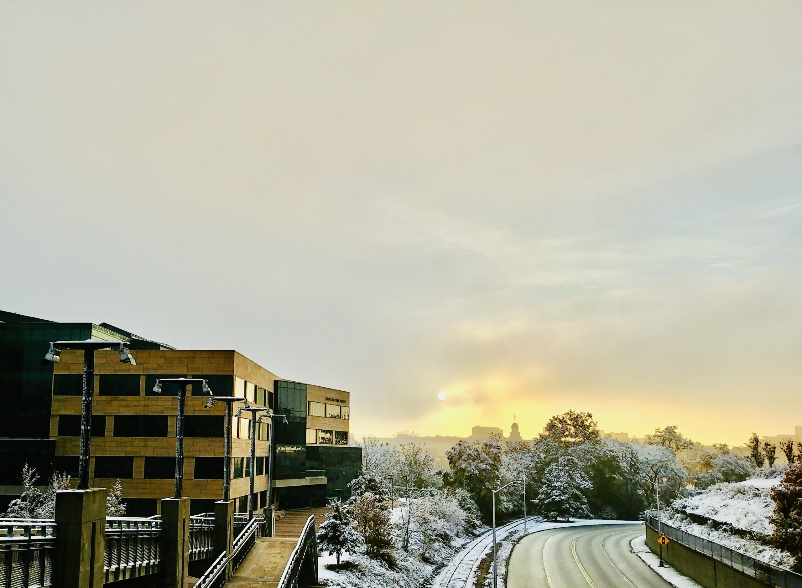 College of Public Health building in winter with the Old Capitol in the distance on an overcast day with snow on the ground.