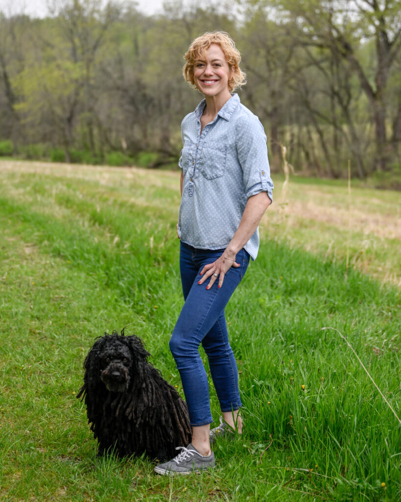 Jenna Gibbs smiling in a grassy area with her black dog.