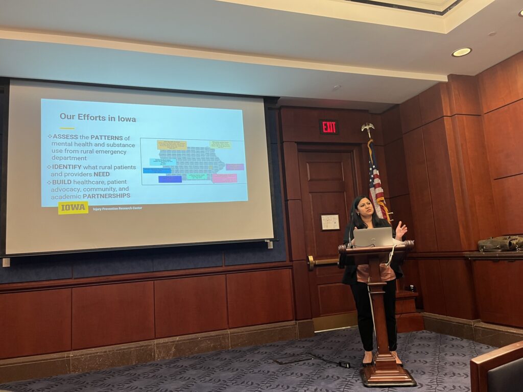 Woman talking at a podium in front of a screen that says, "Our efforts in Iowa."