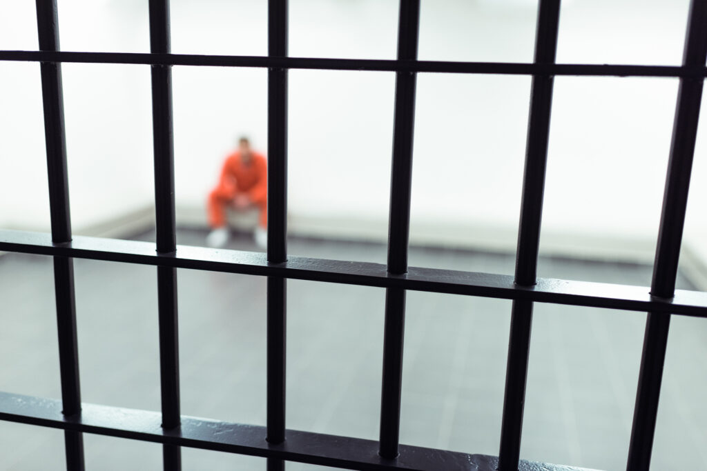 A man in orange clothing sits inside an empty jail room.