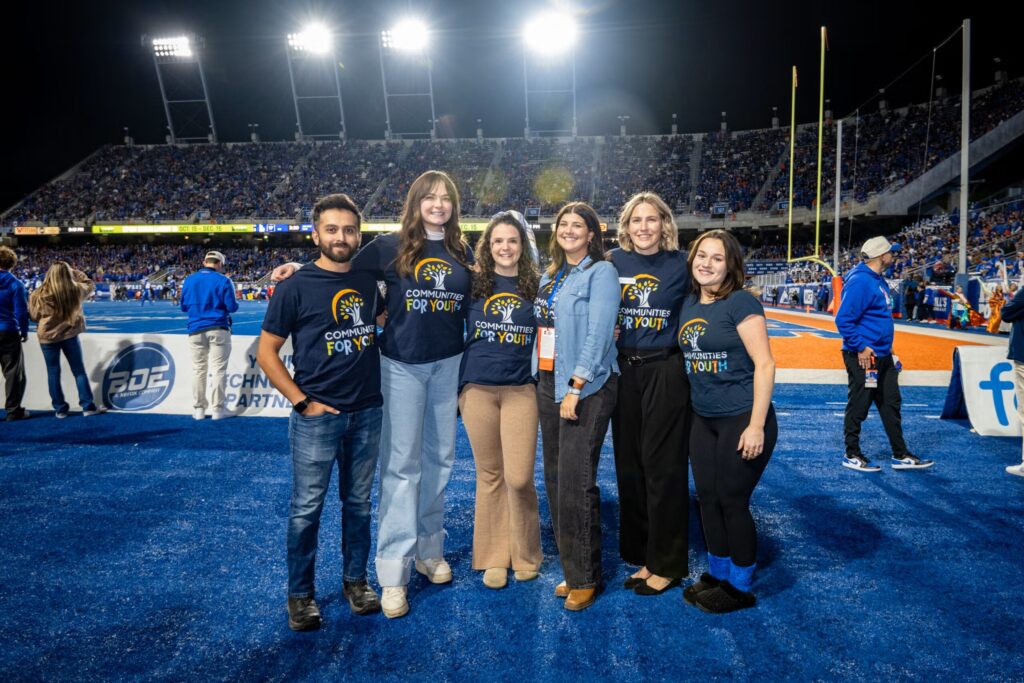 Six people posing on the side of a football field with T-shirts that say "Communities for Youth"